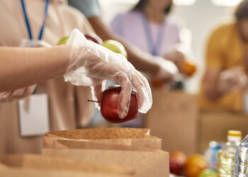 People are lined up placing food items into brown paper bags (Thanksgiving dinners)