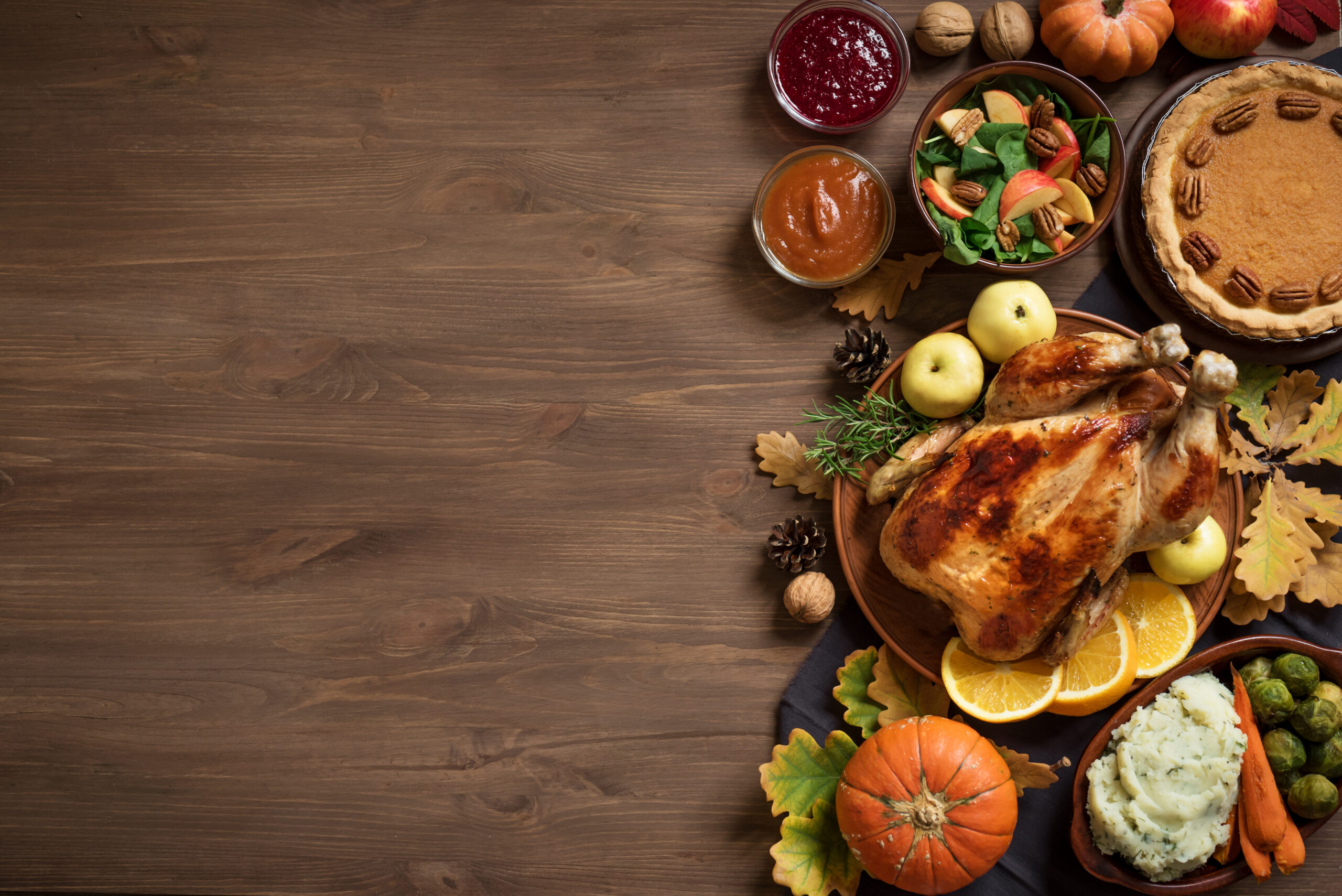 Thanksgiving dinner background with turkey and all sides dishes, pumpkin pie, fall leaves and seasonal autumnal decor on wooden background, top view, copy space.